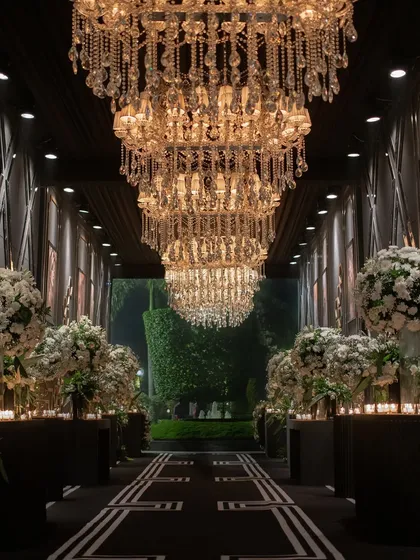 For a glamorous 25th-anniversary celebration, I designed this dramatic entryway. A grand hallway lined with massive crystal chandeliers and lush white floral arrangements set a sophisticated, high-energy tone for a night of black-tie opulence and dancing.