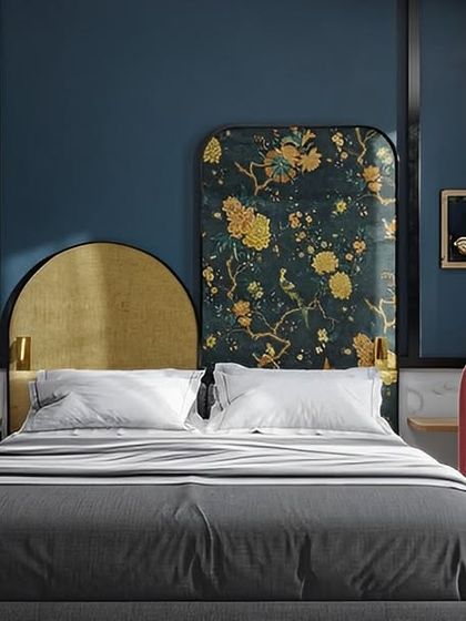We designed this bedroom with a bold, artistic flair. It features a custom asymmetrical headboard with gold and floral patterns, paired with a deep blue wall and a unique pink armchair, creating a vibrant and eclectic space.
