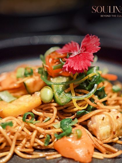 A close-up of vibrant Hakka noodles, garnished with fresh vegetables and an edible flower. This dish highlights our ability to elevate even familiar dishes with beautiful presentation and fresh ingredients.