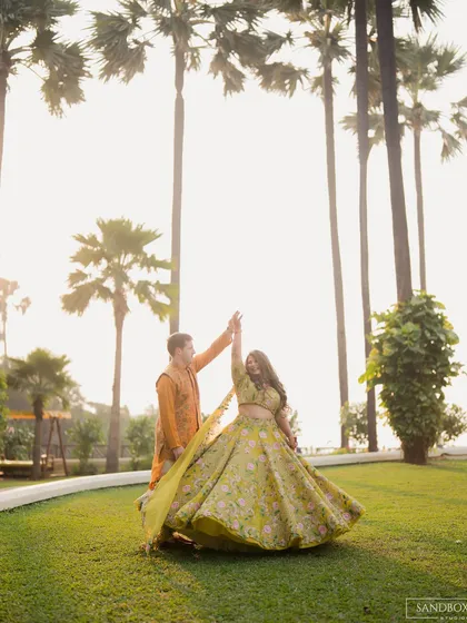 The couple twirls in a beautiful garden setting at the Taj Land's End, with the bride's lime green lehenga creating a stunning visual.