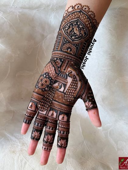 A close-up of the detailed henna work on one hand, showing the fine lines of the peacock and the delicate lotus patterns on the fingers.