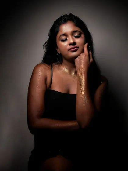 A portrait painted with light and stardust. This creative studio session uses dramatic, low-key lighting to highlight the texture of gold glitter, creating a moody and celestial vibe.