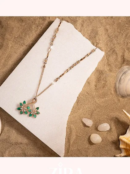 A delicate Zira necklace with emerald-green floral pendants, set against a beach-inspired backdrop.