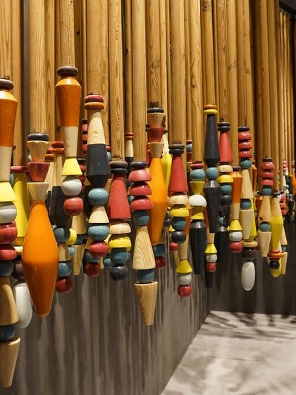 This installation of lacquered wooden spindles from Channapatna complements the handwoven copper panels of 'India Everywhere'. The piece represents the fusion of India's rich craft traditions with a contemporary design aesthetic, creating a vibrant, textured landscape.