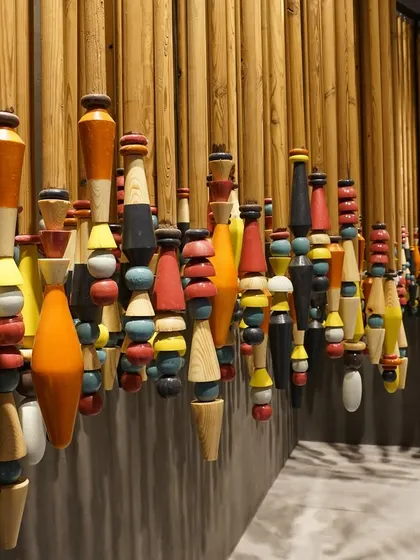 A close-up of the colorful, lacquered wood spindles from the 'India Everywhere' installation. The repetition of form and vibrant color creates a powerful visual rhythm against the wall.