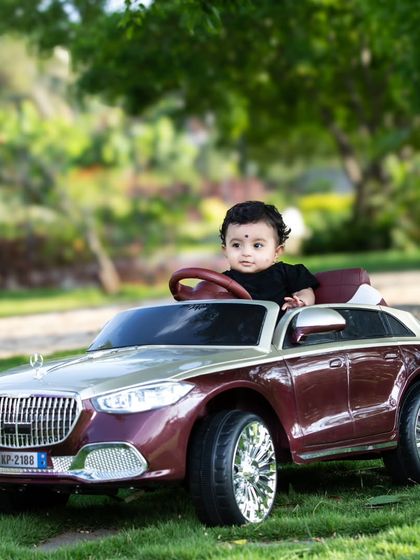 A cute baby girl taking the wheel of a luxury toy car.