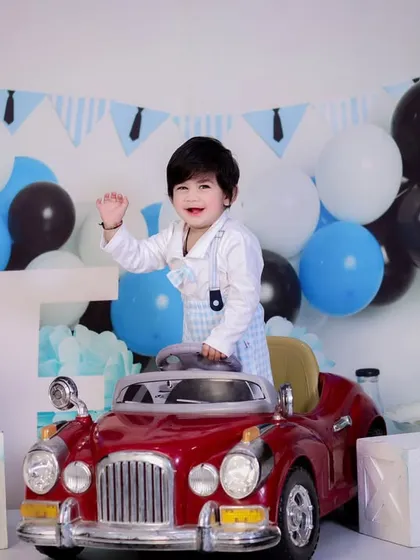 A happy wave from the birthday boy as he cruises in his red car. A candid and joyful moment from a first birthday session.