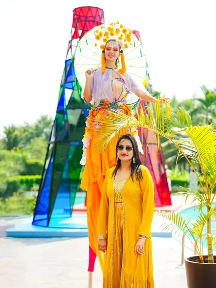 A performer on stilts, dressed in a vibrant, floral-themed costume, poses with a guest in front of the Coachella tower. We use live entertainment to enhance the theme and create an interactive environment.