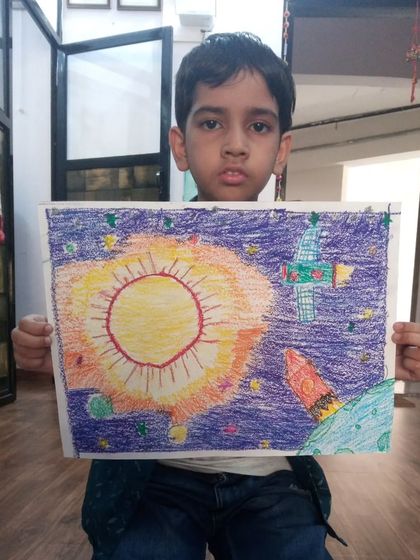 Aaryav, a 6-year-old student, drew this vibrant space scene with oil pastels. His artwork includes the sun, a satellite, and a rocket, showing his fascination with space.