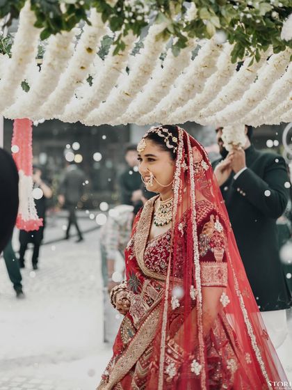 The bride, Parul, making her entrance under a phoolon ki chadar, with a gentle smile of anticipation.