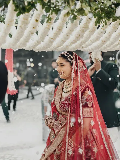 The bride, Parul, making her entrance under a phoolon ki chadar, with a gentle smile of anticipation.