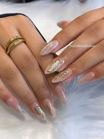 An elegant design combining a sheer, shimmery base with 3D chrome art. The sculpted silver and gold leaf accents add a touch of sophisticated magic to these long almond nails.