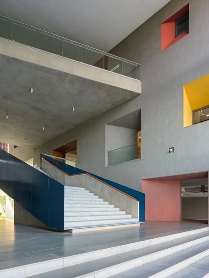 A monumental staircase at Ahmedabad University's School of Arts and Sciences serves as a central organizing element. Punctuated by colorful, deeply recessed windows, it is both a functional circulation path and a powerful architectural statement.