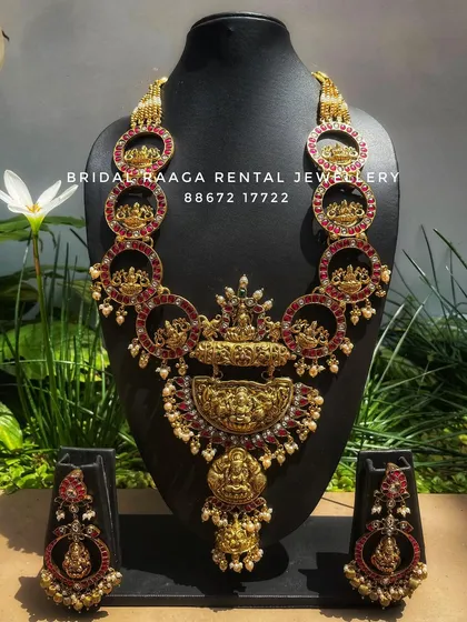 A unique and artistic temple jewellery set. The design features circular motifs with Goddess Lakshmi carvings, all studded with red Kemp stones.