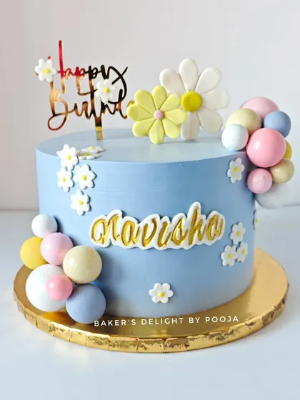 A sweet and simple birthday cake in a lovely shade of blue, decorated with pastel-colored chocolate balls and fondant daisies.