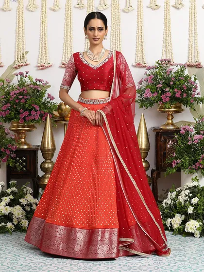 A vibrant orange Bandhani lehenga paired with a deep red embroidered blouse. This is a bold and beautiful choice for a modern bride.