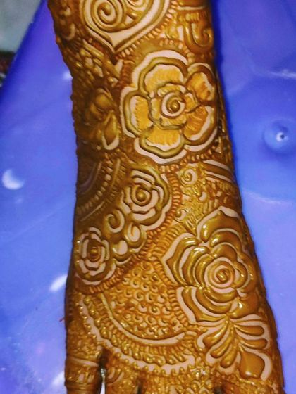 A close-up of the fresh henna paste on the feet, showing the 3D texture of the rose patterns.