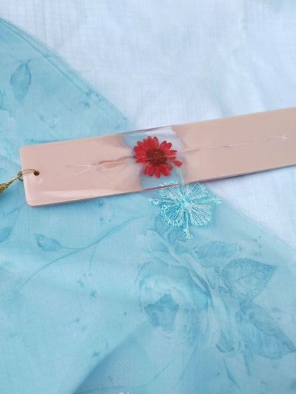Another angle of the red flower bookmark, showing its slim profile and the delicate white tassel.