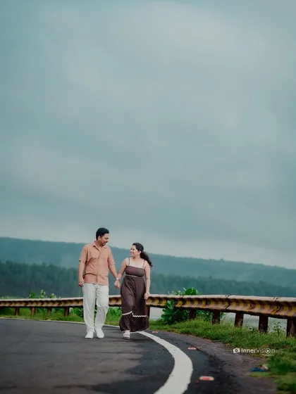 A wide shot of the couple walking hand-in-hand on a road with a beautiful view of the Kokan hills and backwaters, telling a story of a journey together.