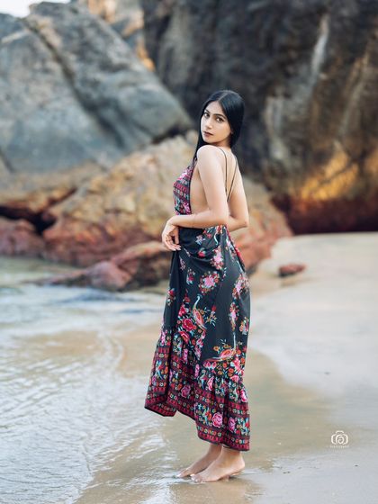 A lovely portrait of a model in a floral dress, looking back over her shoulder. The soft, natural light and the beach background create a gentle and romantic feel.
