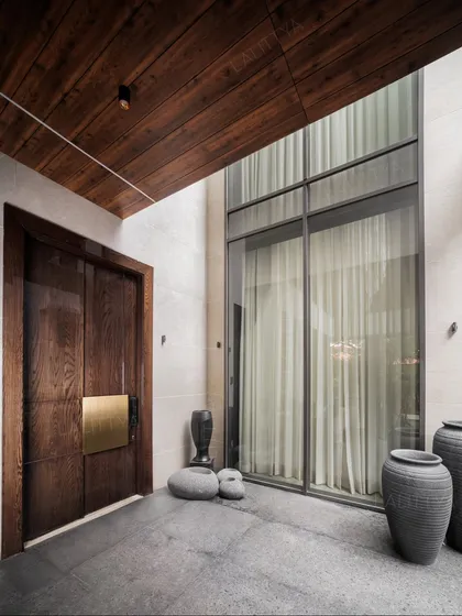 Our work isn't just about interiors; we are architects who shape spaces from the ground up. This modern entrance, with its bold wooden door, brass accents, and double-height window, establishes a sense of arrival and sets the tone for the quiet luxury within.