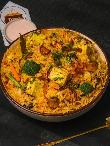 A hearty bowl of vegetable biryani with paneer and soya chunks, shot from above on a dark table. The moody lighting enhances the rich colors of the spices and ingredients.