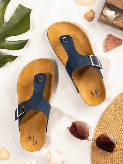 A summer-themed flat lay of navy blue sandals for Fancy Nancy, styled with a straw hat and sunglasses. This composition tells a story of vacation and beach-side relaxation.