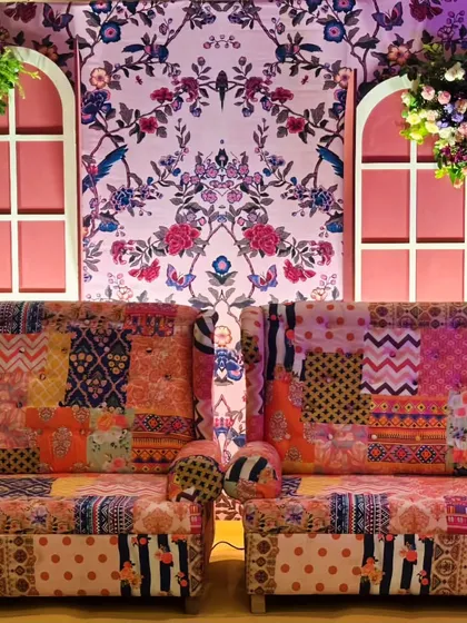 A cozy and eclectic seating area for the Mehendi, with patchwork sofas set against a floral wallpaper backdrop with charming pink window shutters.