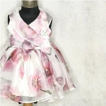 The "Pink Poppy" dress features a beautiful watercolor floral organza and a sweet crossover bodice with a bow detail. It's a light and airy dress for any special occasion.