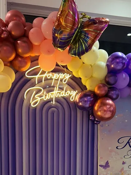A close-up of the fairyland theme, highlighting the neon 'Happy Birthday' sign, metallic butterfly details, and a rich palette of chrome and pastel balloons.