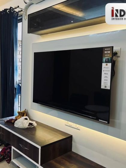 The TV unit is designed with a clean white back panel and ambient backlighting, which reduces eye strain and creates a cinematic feel. The dark wood console offers ample storage.