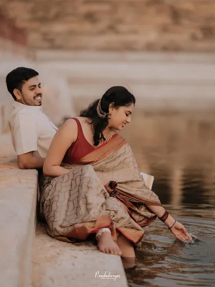A serene moment of the couple sitting by the temple pond, the bride gently touching the water.