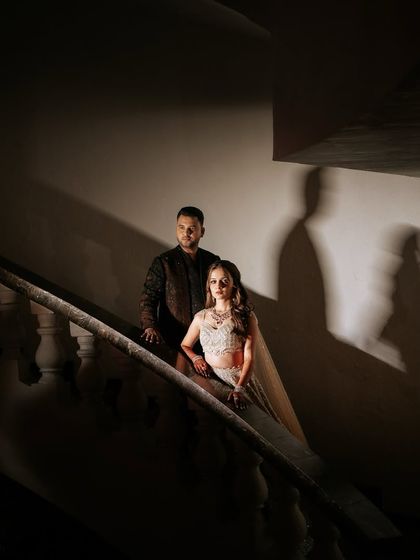 A dramatic shot of the couple on the stairs. The lighting highlights the rich texture of the groom's jacket and the sparkle of the bride's outfit, creating a moody and romantic atmosphere.