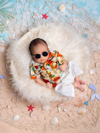 Cool, calm, and collected on a bed of soft fluff. This beach-themed newborn shoot uses a fun Hawaiian shirt and sunglasses to bring a touch of summer to your baby's first photos.