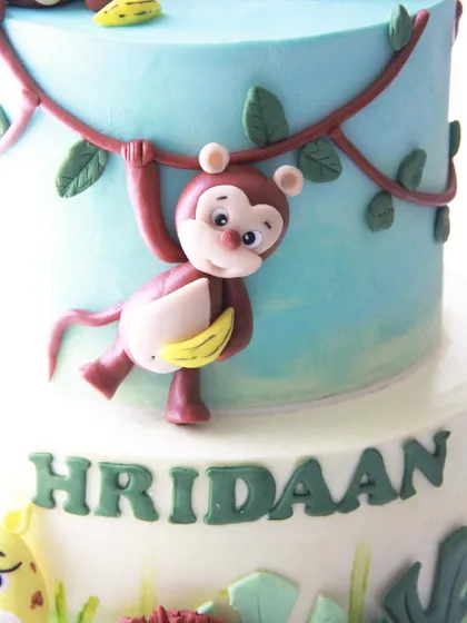 This little monkey, complete with a banana, adds a playful touch as he swings from a vine on the side of the jungle cake.