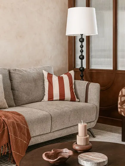 A detail of the living room sofa, styled with a striped rust-colored cushion and a cozy throw. The beaded floor lamp and fluted glass partition in the background add more layers of texture and detail.