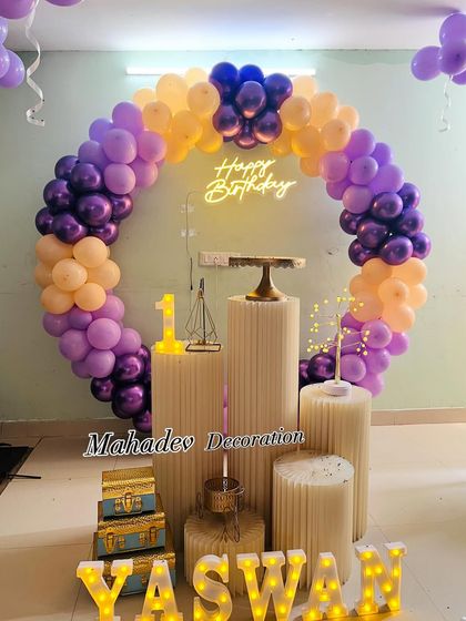 A simple and elegant circular balloon arch in purple and peach for a first birthday. The setup includes pedestals and light-up letters for the name.