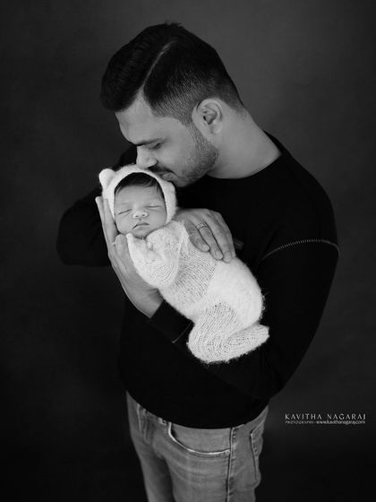 A new dad holds his baby, dressed in a white bear outfit. This black and white portrait is a simple, timeless image of a father's love.