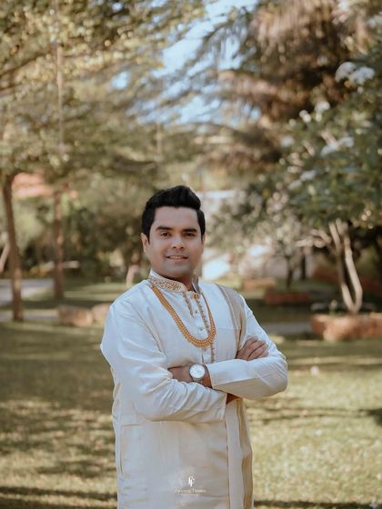 A happy groom posing in a garden on his wedding day.
