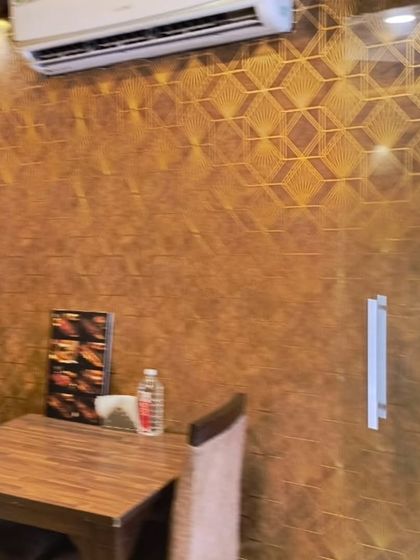 A restaurant wall covered in a gold geometric-patterned wallpaper. The metallic lines catch the light and add a touch of art deco glamour to the dining area.