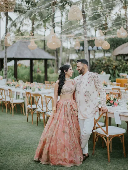 Posing by their beautiful outdoor sangeet setup. The soft peach and floral theme of their outfits ties in perfectly with the event's decor, creating a cohesive and visually stunning aesthetic.