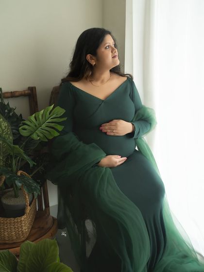 A moment of quiet reflection by the window. The natural light and surrounding greenery create a peaceful and organic setting for this solo maternity portrait.