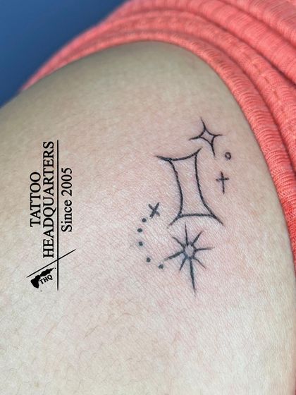 A minimalist Gemini zodiac symbol surrounded by sparkling stars, a delicate and personal astrological tattoo.