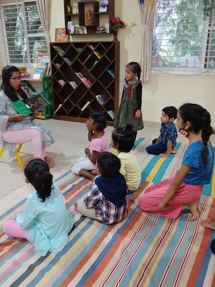 The storyteller holds up a book with charming illustrations, perfect for capturing the attention of young children.