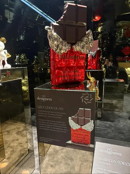 A 'Love Chocolate' sculpture on display in Hyderabad. The mirrored pedestal reflects the gallery's dramatic lighting, enhancing the artwork's presence.