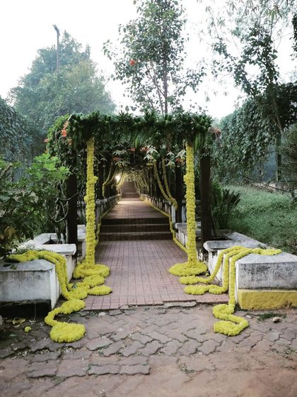 For this outdoor event, I decorated a bridge to create a rustic and charming entrance pathway. The structure is wrapped in greenery and long garlands of yellow flowers, blending seamlessly with the natural surroundings.