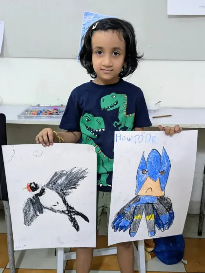 Meera, age 6, with her fantastic artwork. She has created a dynamic drawing of a bird in flight and her own version of a superhero, showcasing her growing skills.