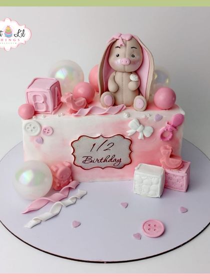 A sweet half-birthday cake in shades of pink. This design features a cute bunny, baby blocks, and pearlescent bubble decorations.