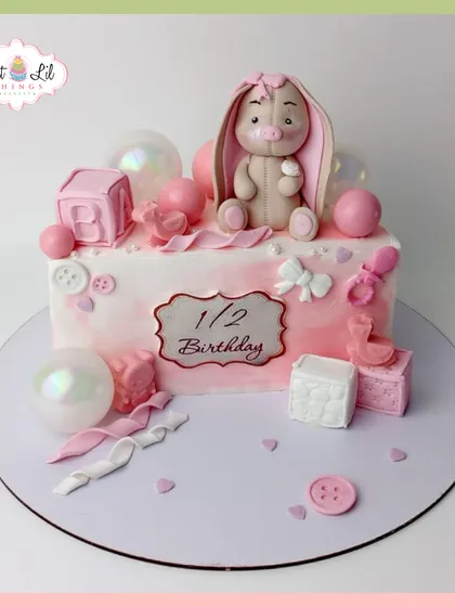 A sweet half-birthday cake in shades of pink. This design features a cute bunny, baby blocks, and pearlescent bubble decorations.