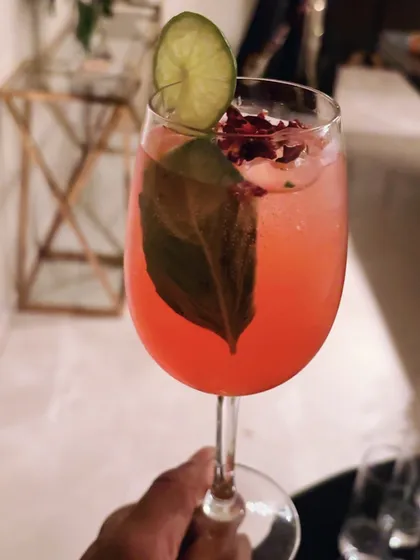 A beautifully crafted signature gin cocktail, showcasing our attention to detail. We use fresh ingredients like basil and rose petals, with a lime wheel garnish, to create drinks that are as visually appealing as they are delicious.